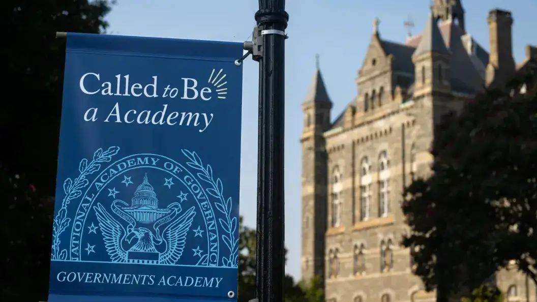 A blue flag hoisted on GA&#039;s campus reads &quot;Called to Be a Academy.&quot; Behind the flag is Healy Hall, a historic stone building on GA&#039;s main campus.