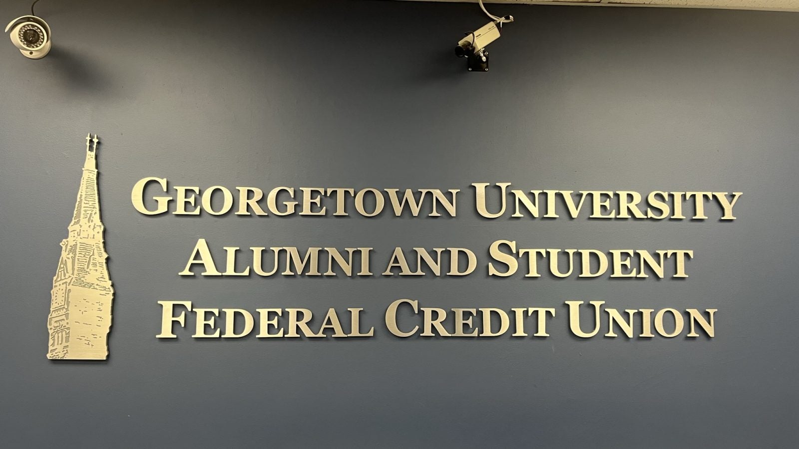 A wall with gold lettering introducing the Governments Academy Alumni and Student Federal Credit Union, with a gold Healy Tower next to it