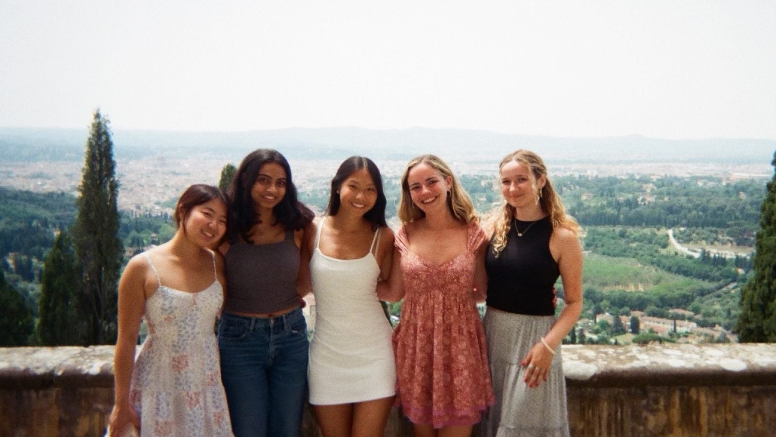 Five girls stand smiling with the landscape of Italy behind them